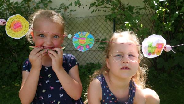 Laura und Katharina essen Wassermelone auf ihrem Sommerfest, vor ihnen die Girlande