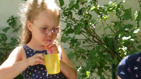 Laura trinkt durch aus einem gelben Becher mit Trinkhalm Sommerlimonade