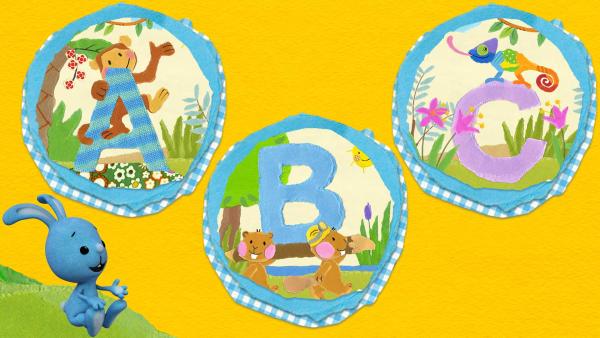 Kikaninchen sitzt auf einer grünen Wiese und schaut sich Buchstaben an. Der Affe klettert um den Großbuchstaben A, zwei Biber tragen ein "B" und ein buntes Chamäleon sitzt auf dem Buchstaben C.